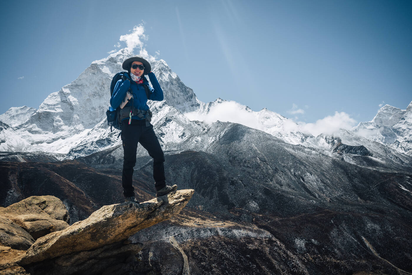 Grace on a rocky perch with Ama Dablam pyramid filling the sky behind