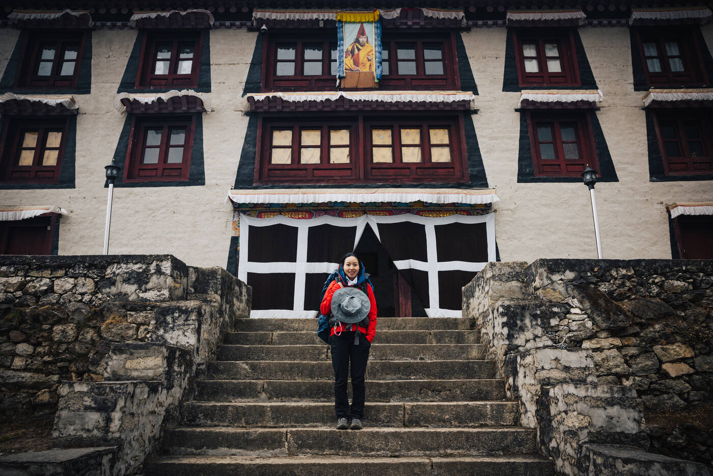 Grace in a red jacket on the entrance steps of Pangboche Monastery, the multi-story stone temple rising behind her