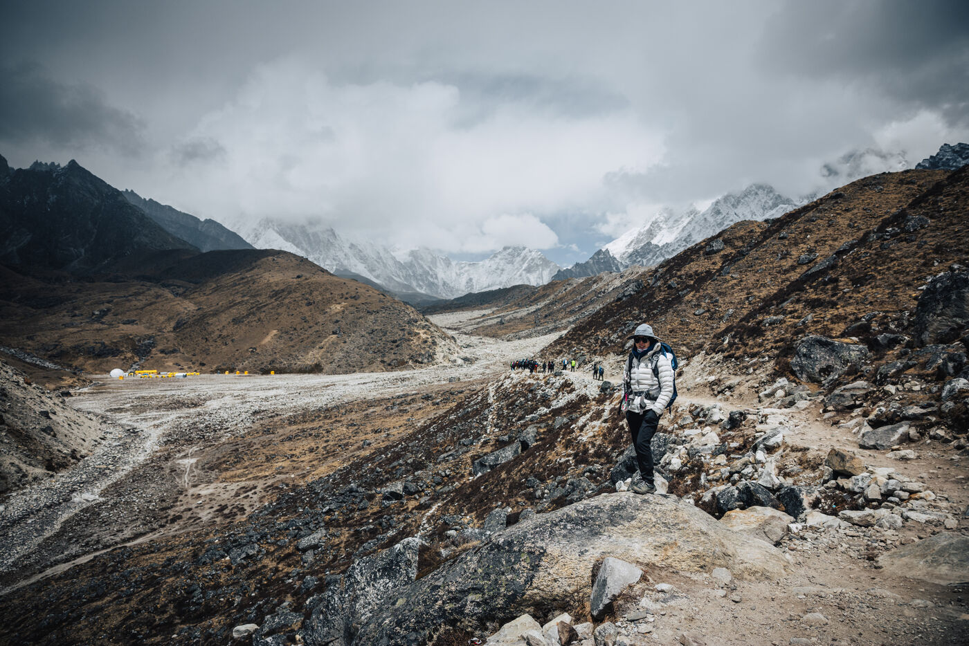 Grace on a moody trail above a cluster of yellow lodge roofs on the valley floor, low clouds clinging to the high peaks beyond