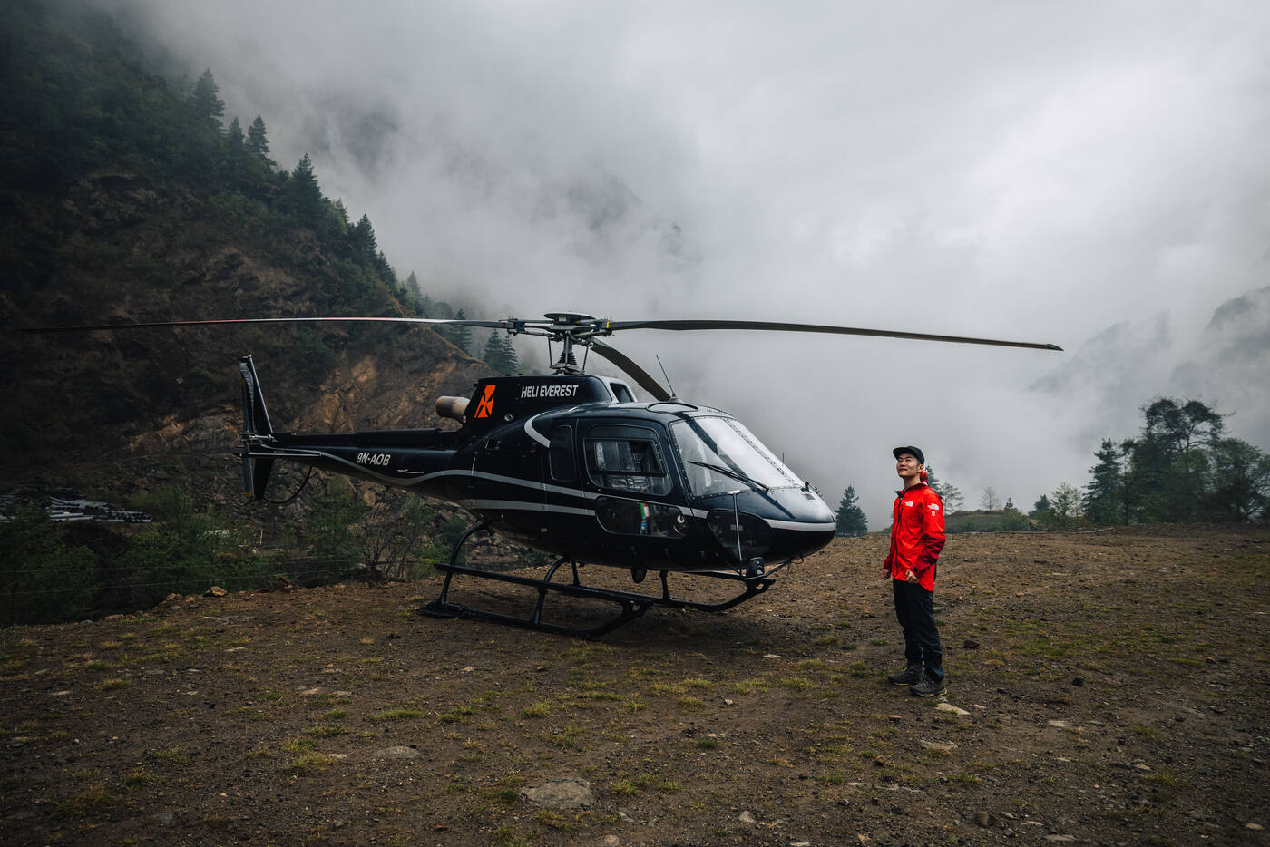 Jason standing next to the helicopter at the Surke landing zone in a red mountaineering jacket