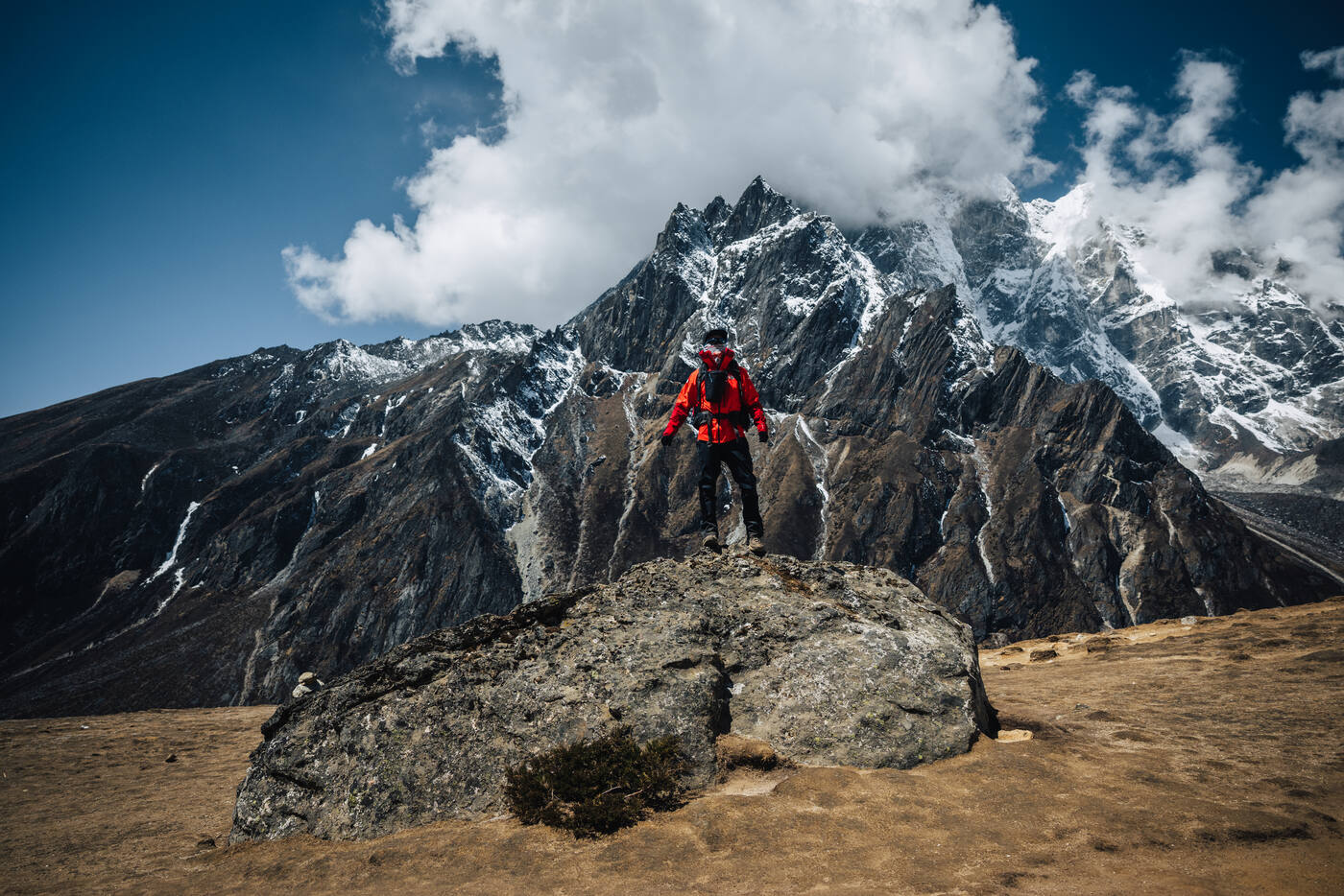 Jason on a lone boulder above Dingboche, a jagged dark Cholatse ridge looming in the clouds behind