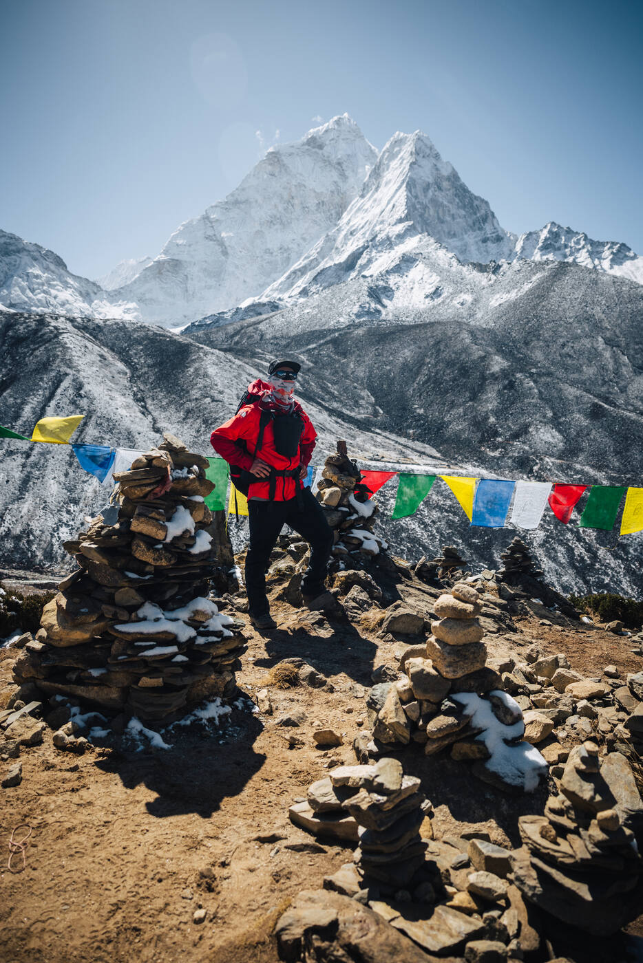 Jason in red among stone cairns and prayer flags on the Nangkartshang ridge with Ama Dablam rising behind