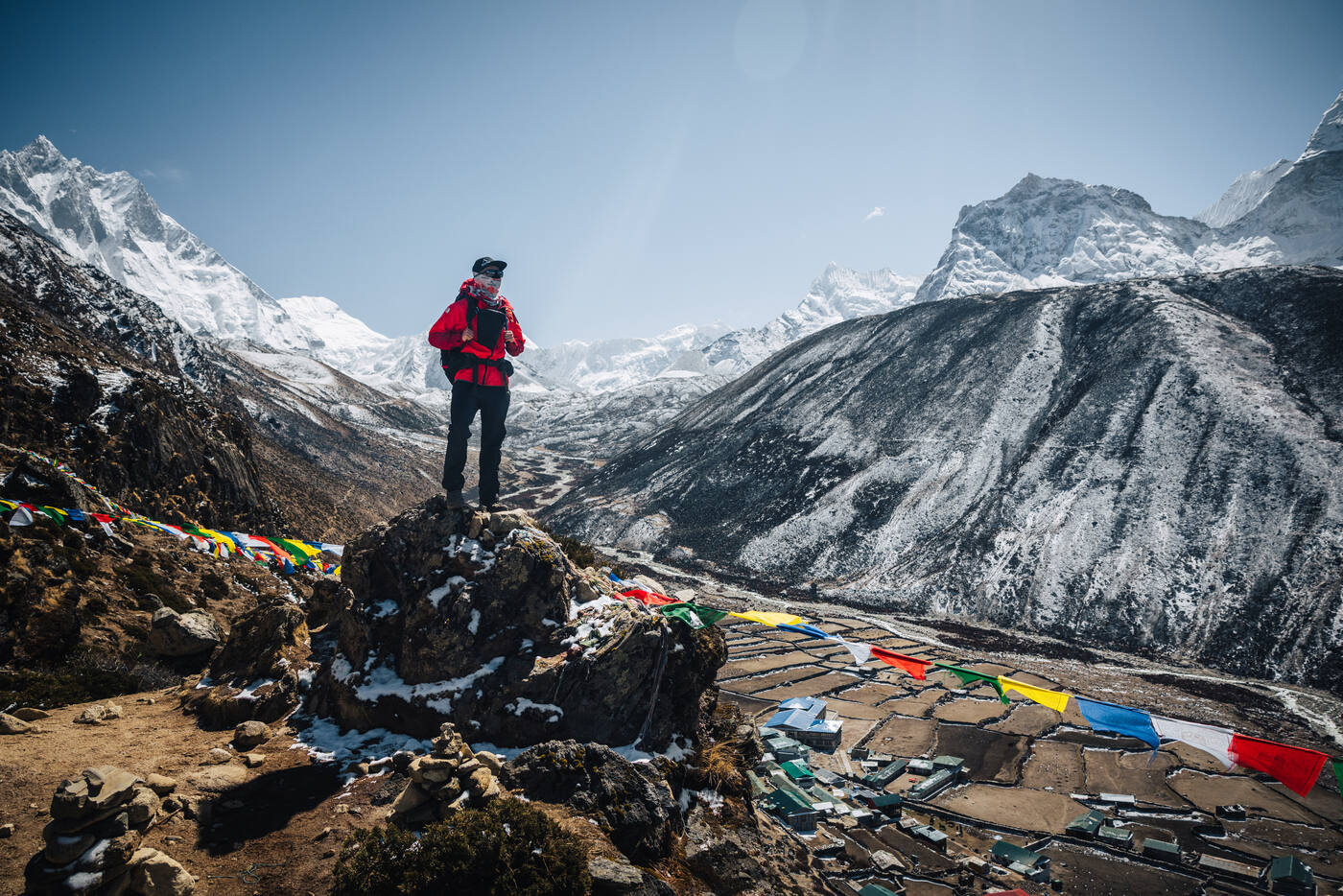 Jason on a rocky perch above Dingboche with prayer flags strung across the valley, terraced fields and snow peaks spread below