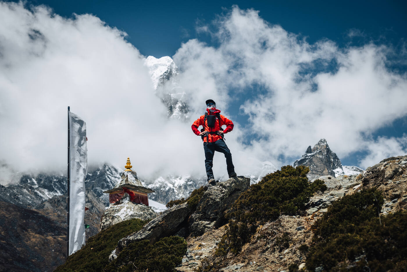Jason atop a ridge shrine in a red jacket, clouds roiling around snow peaks behind — the Nangkartshang viewpoint