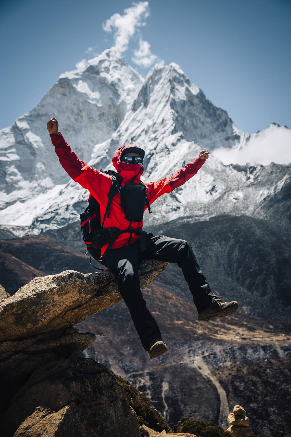 Jason triumphant on a rocky perch with both arms raised, Ama Dablam's pyramid peak rising through the clouds behind