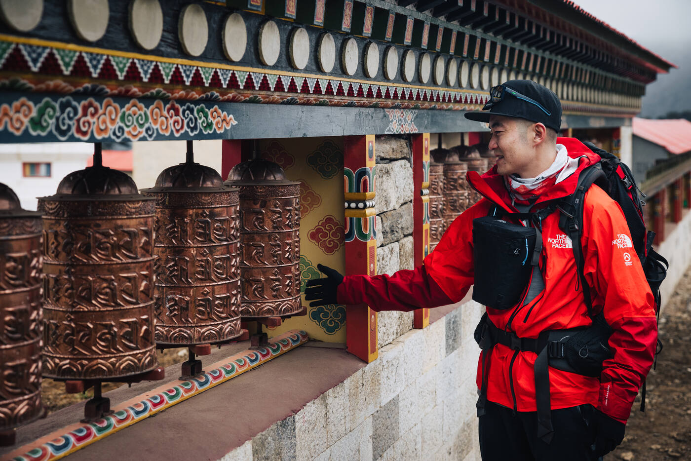 Jason in a red North Face jacket spinning a row of copper prayer wheels at Tengboche