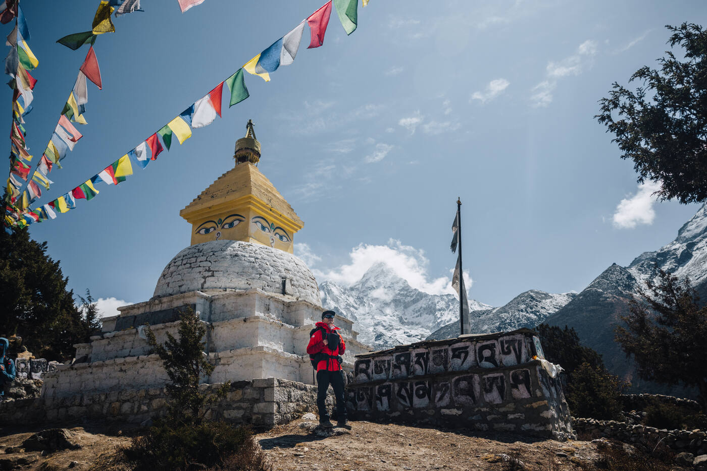Jason beneath strings of prayer flags at a hilltop stupa, Ama Dablam looming in the distance