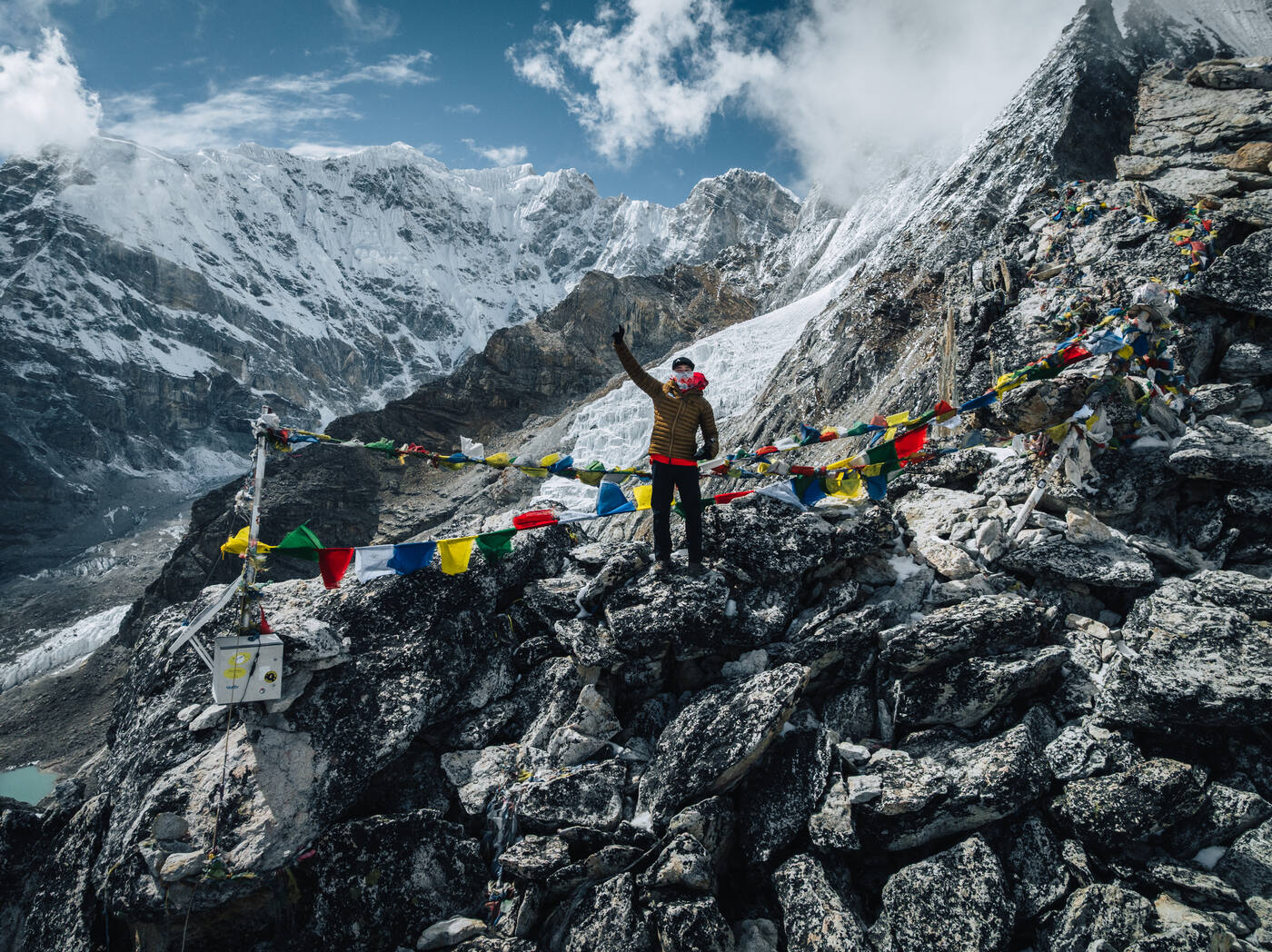 Yellow-puffy trekker at a prayer flag viewpoint above the Khumbu Icefall, Lhotse and Nuptse's wall rising behind