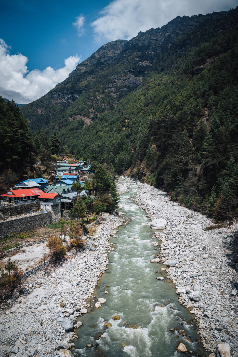 The Dudh Koshi River cutting through a milky channel beside a small lower-Khumbu village of red-and-blue rooftops