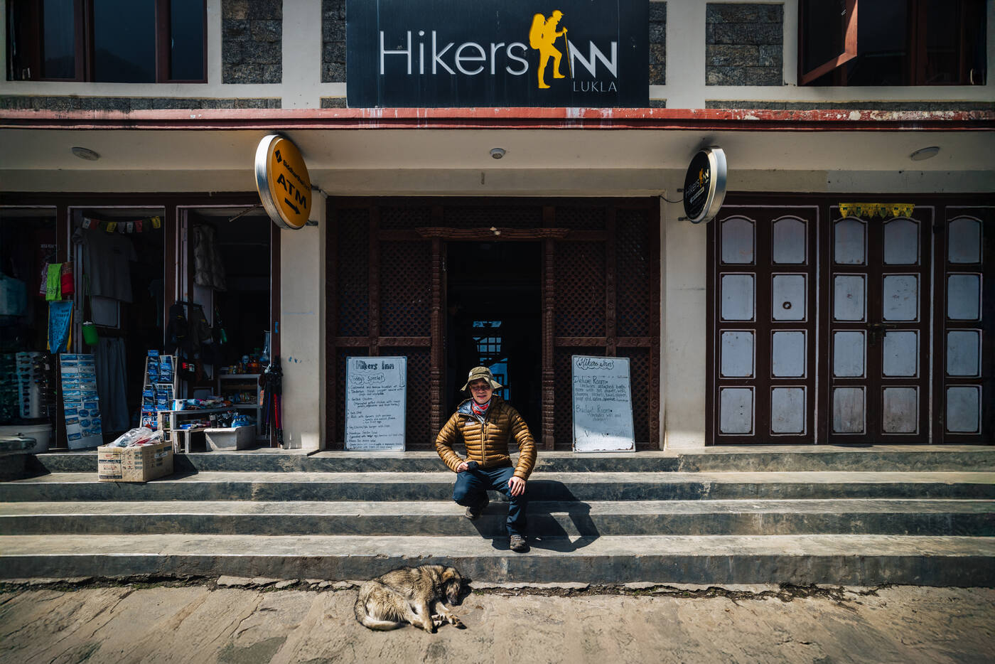 Jason sitting on the steps of Hikers Inn Lukla in the morning sun with a sleeping dog at his feet