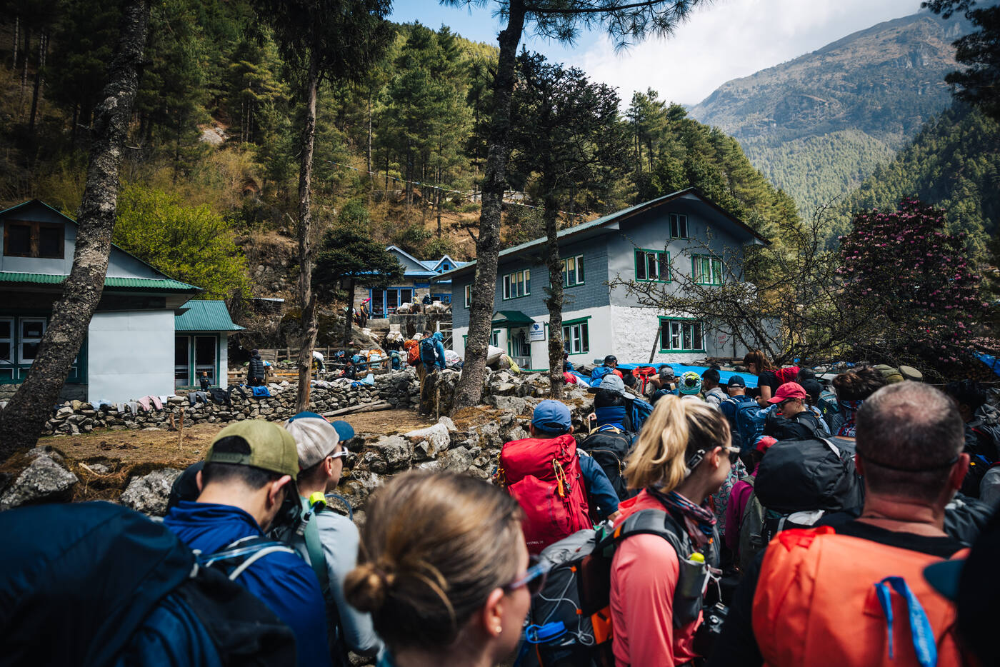 A crowd of trekkers and porters waiting at a checkpoint outside the green-and-white Monjo lodge