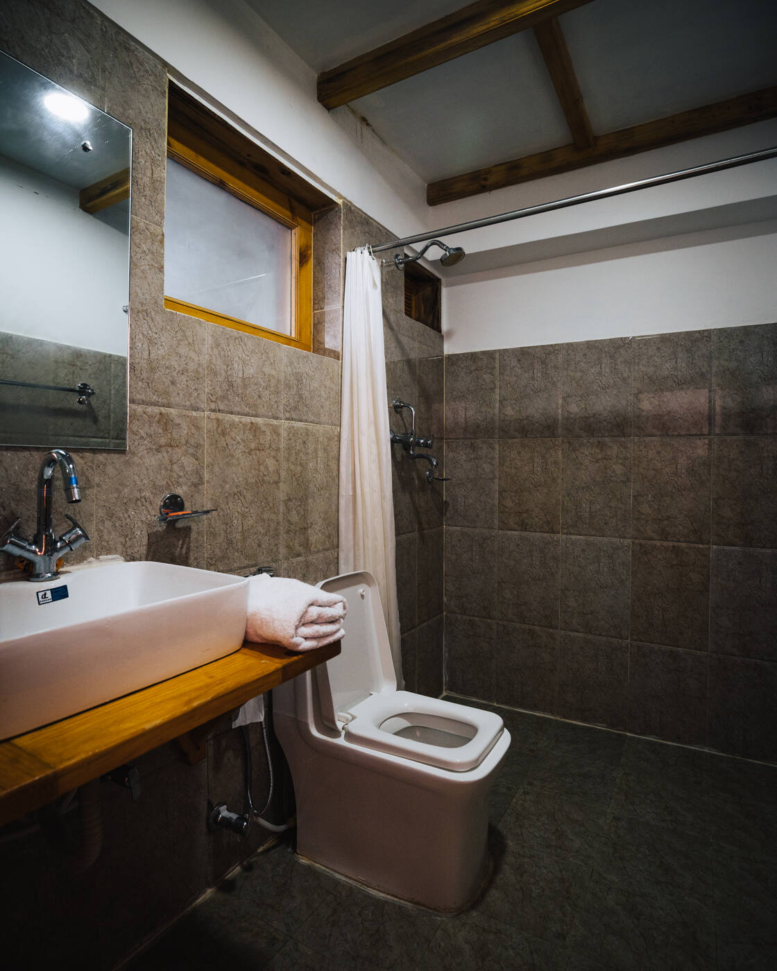 The modern tiled bathroom at Hotel Camp de Base — sink, towel, flush toilet, and shower in tan stone tile
