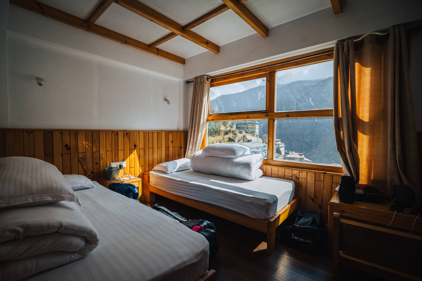 Twin-bed lodge room at Hotel Camp de Base — crisp white linens, warm wood paneling, a large window overlooking Namche