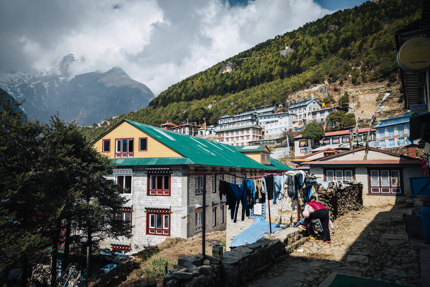 A Namche rest-day scene — laundry drying on a line, green-roofed lodge below, the colorful Namche bowl climbing the hill behind