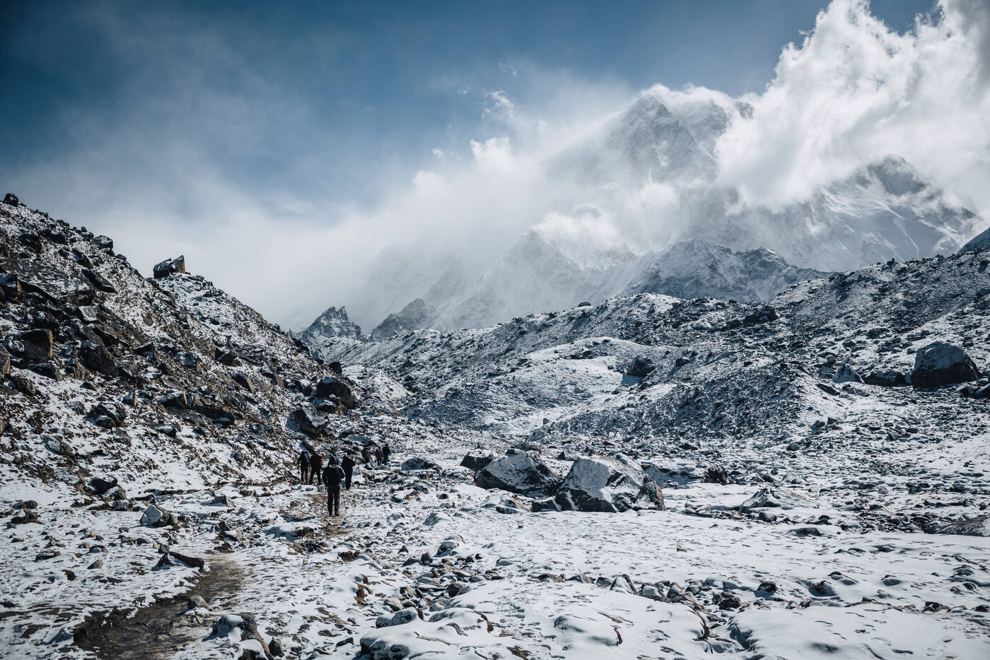 Trekkers walking a snowy moraine trail toward cloud-wrapped peaks — the alpine zone above Thukla