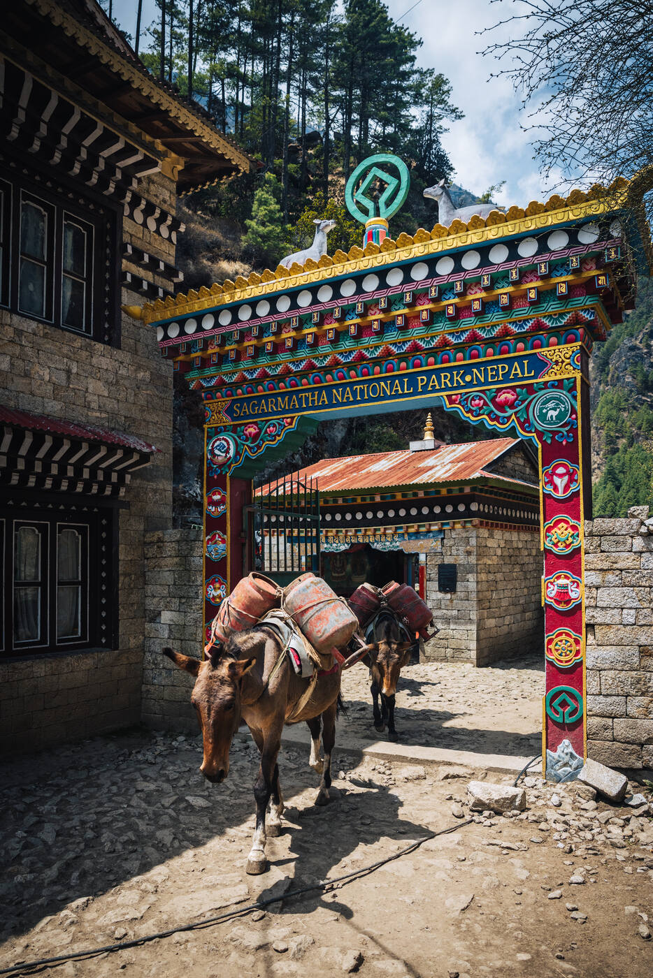 A pack mule loaded with goods walking through the Sagarmatha National Park gate, painted snow lions perched above