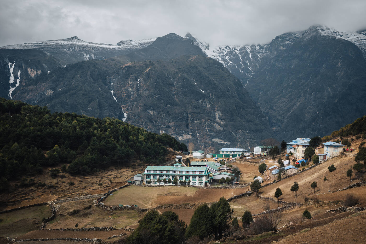 Pangboche village terraced into the hillside, teal-roofed lodges clustered below waterfall-striped cliffs and snow ridges