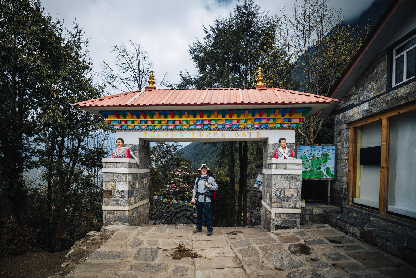 Trekker beneath the ornate Pasang Lhamu Memorial Gate, the painted arch marking the start of the trail out of Lukla