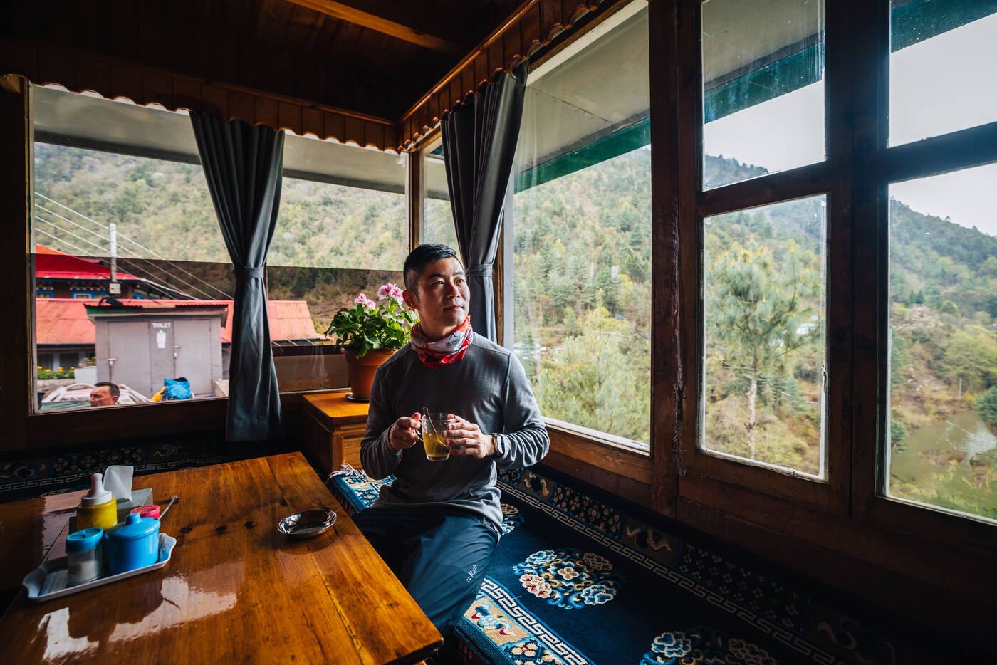 Person sitting inside a mountain lodge with large windows overlooking the river valley below