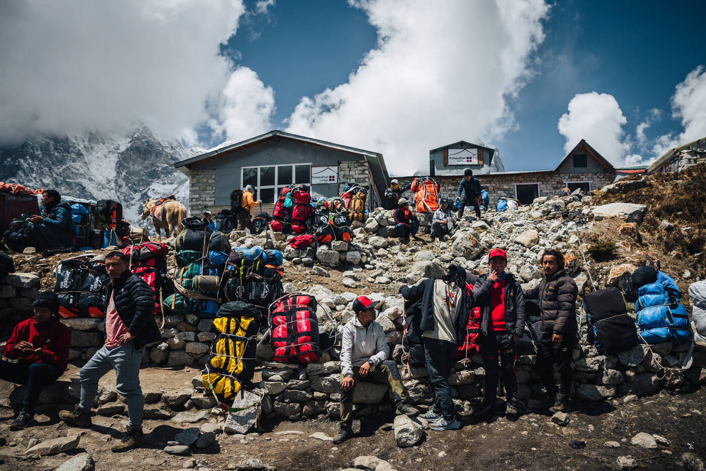 Porters and trekkers gathered at the Lobuche rest stop with duffels and packs piled around the stone lodges