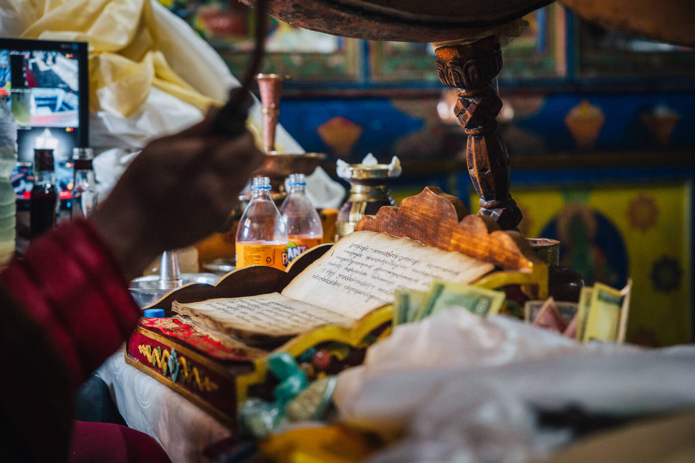 A monk's hand turning the pages of a Tibetan prayer book on an ornate altar during the Puja