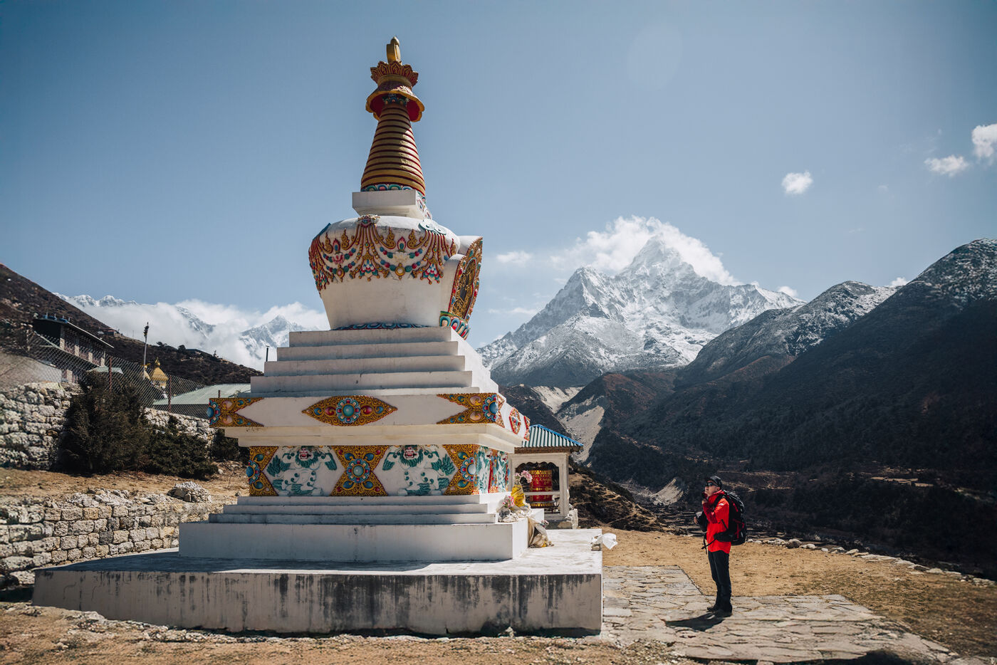 A trekker in red pausing beside a tall white stupa with Ama Dablam looming to the right