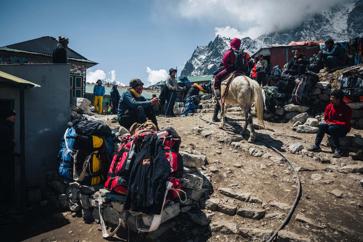 Lobuche porter plaza — a trekker on a horse, rest-stop packs piled on stone walls, rocky slopes rising behind