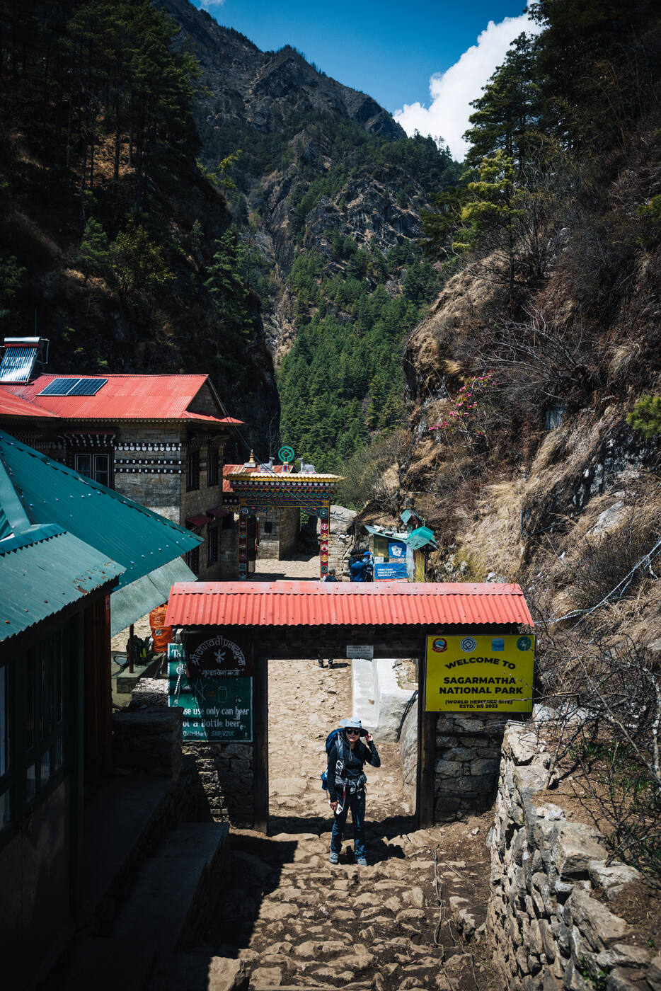 Approach to the Sagarmatha National Park welcome arch — red-roofed entry buildings tucked beside a rocky cliff face
