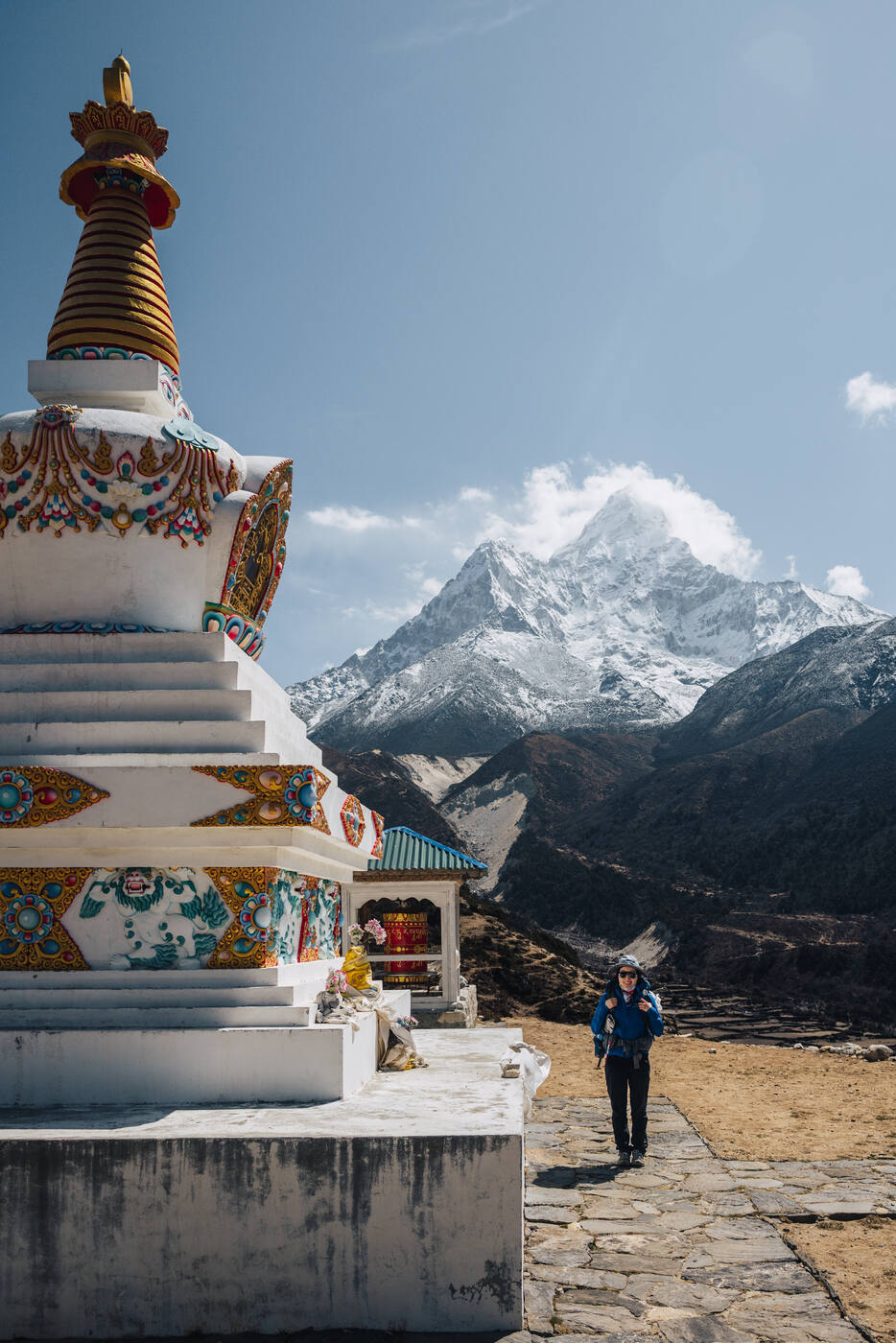 A trekker walking past an ornate white-and-gold stupa with Ama Dablam rising behind