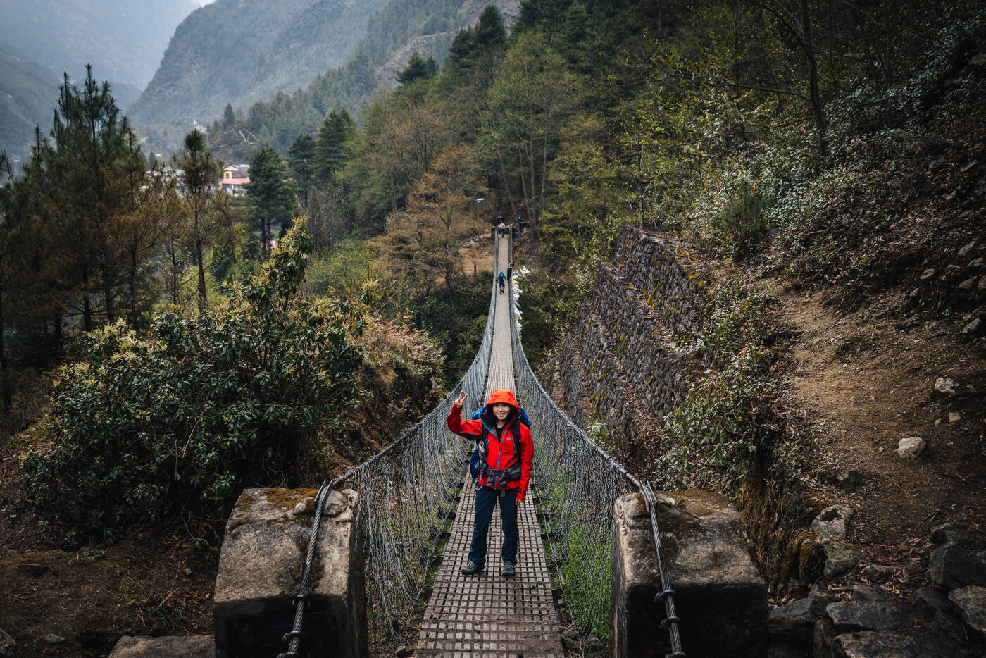 Trekker in a red jacket crossing a suspension bridge over the Dudh Koshi River gorge