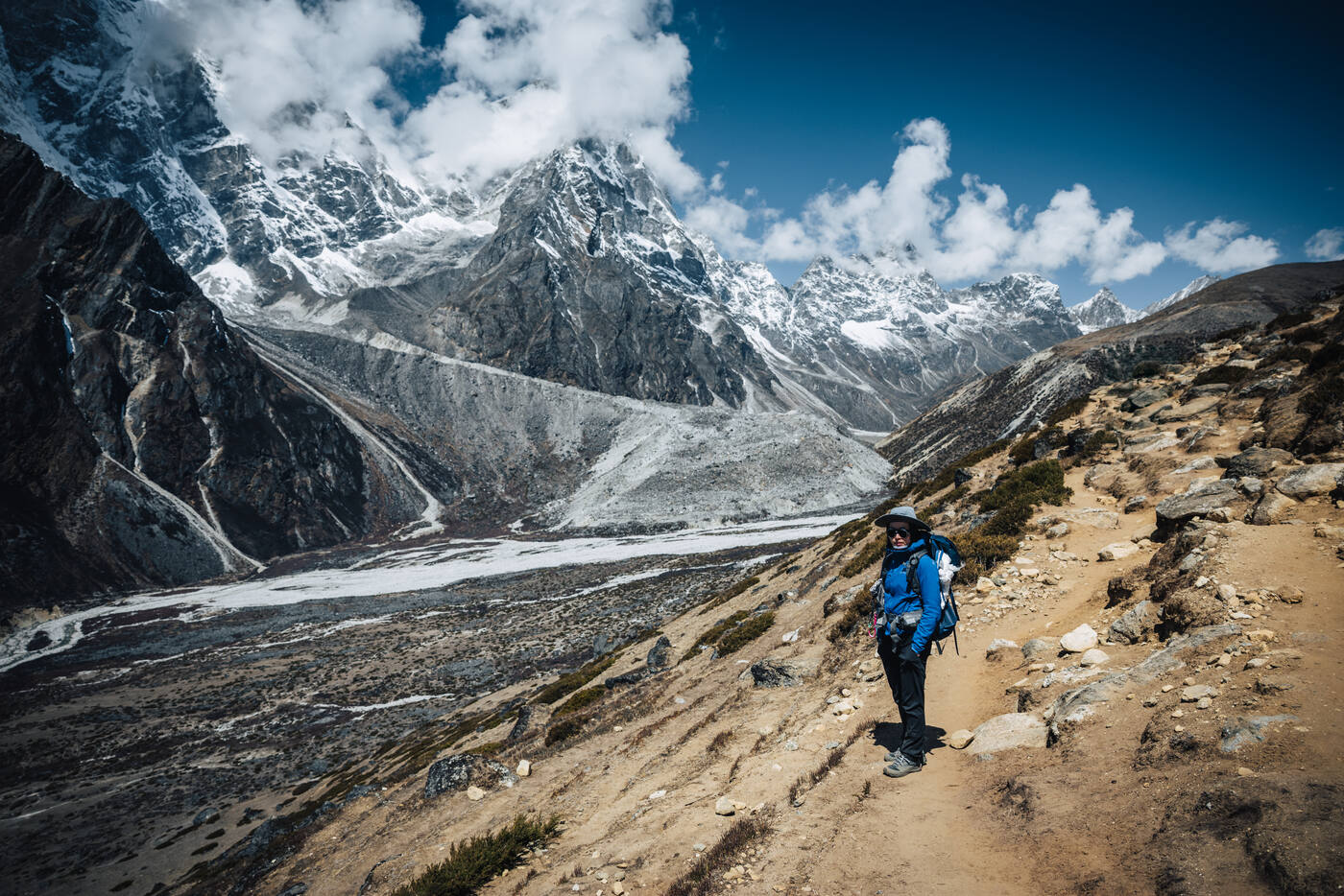 Trekker in blue puffy on a rocky trail above the Thukla valley, Cholatse and Taboche pyramids rising behind