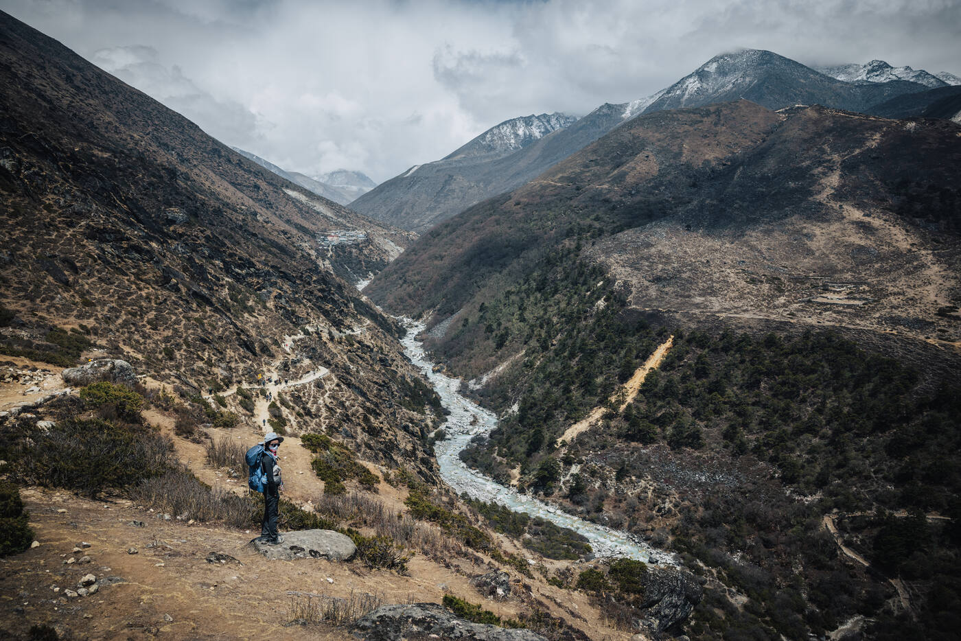 Climber standing on a rocky overlook above the Dudh Koshi river canyon with snow peaks behind