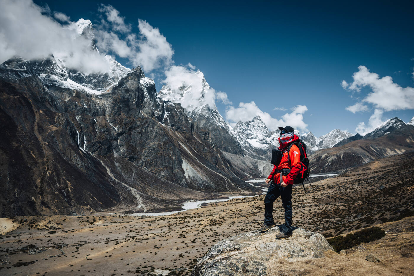 Trekker in red on a rocky perch above Dingboche valley, snow peaks of the Cholatse-Tabuche group rising behind