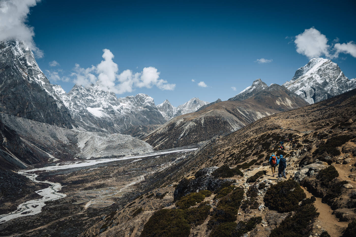 Three trekkers on the high alpine trail toward Lobuche — moraine, glacier streams below, snow peaks all around