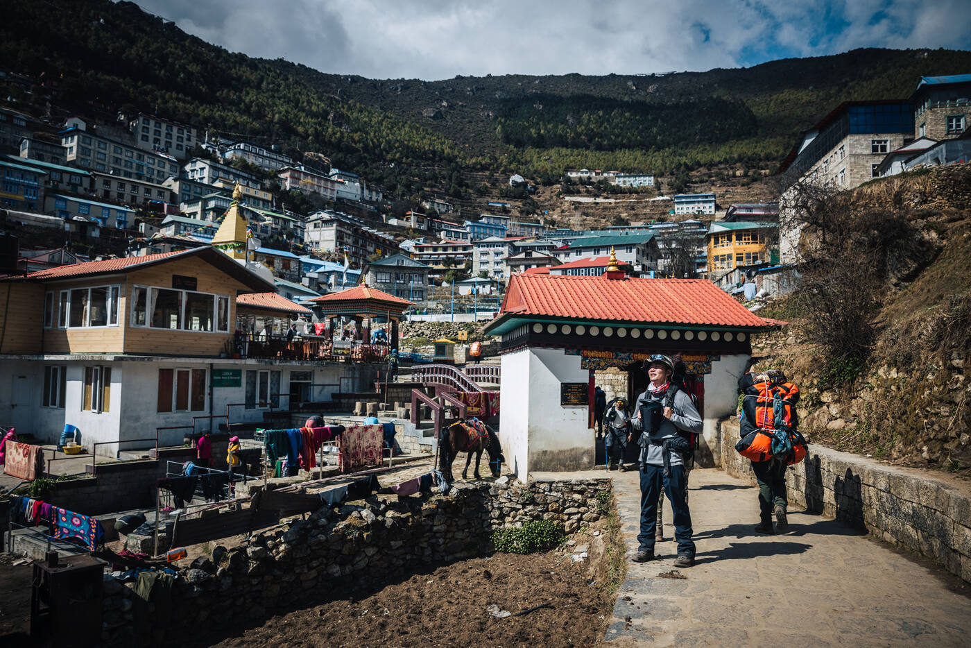 Trekkers with packs passing a small Namche chorten on the trail up from town