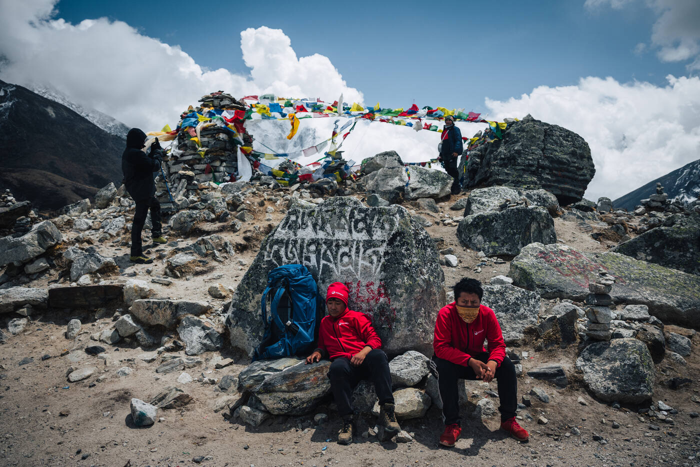 Trekkers resting among massive boulders with mani carvings and prayer flag piles on the Thukla ridge