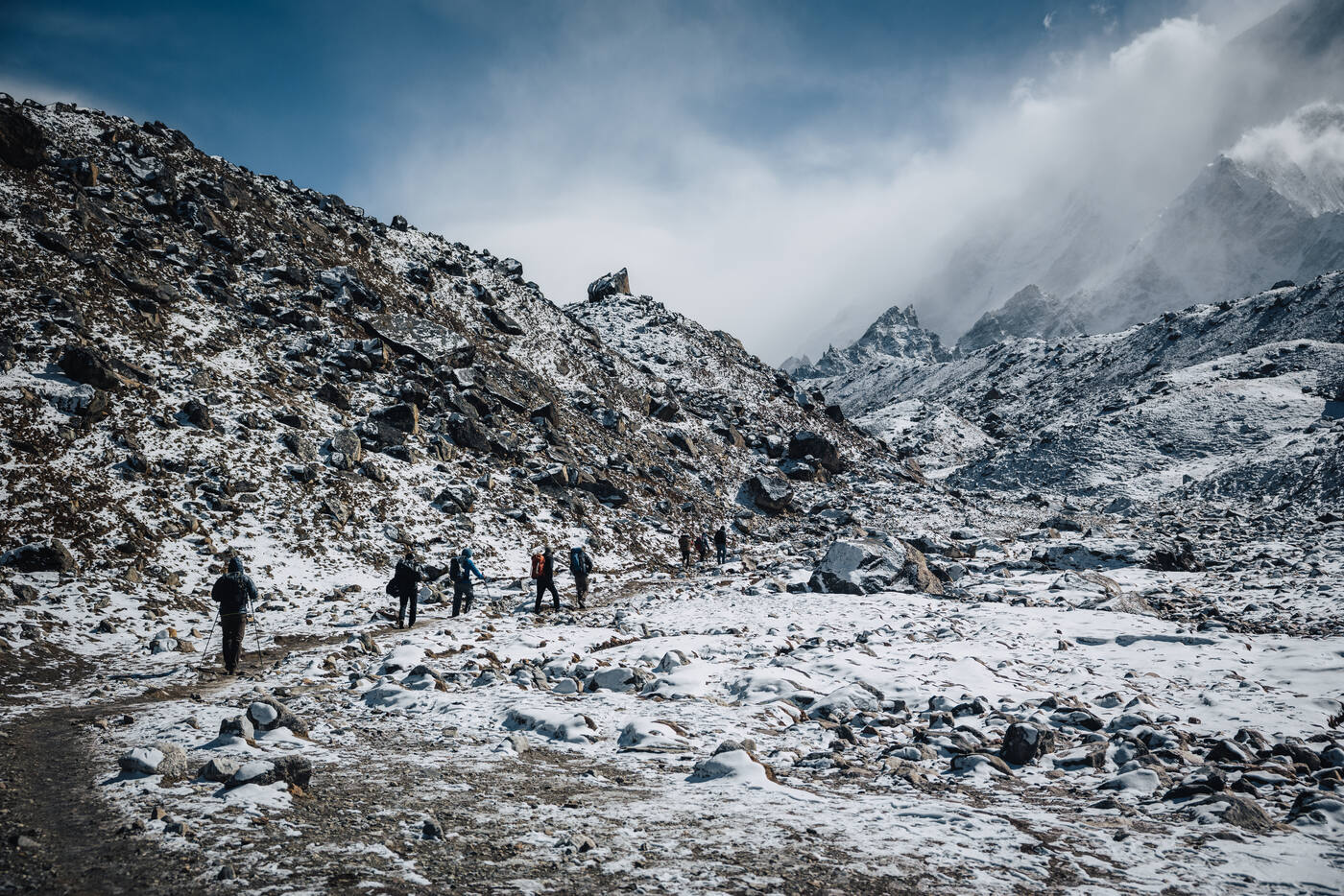 Trekkers crossing the snowy moraine with cloud-wrapped peaks ahead — the approach to Gorak Shep