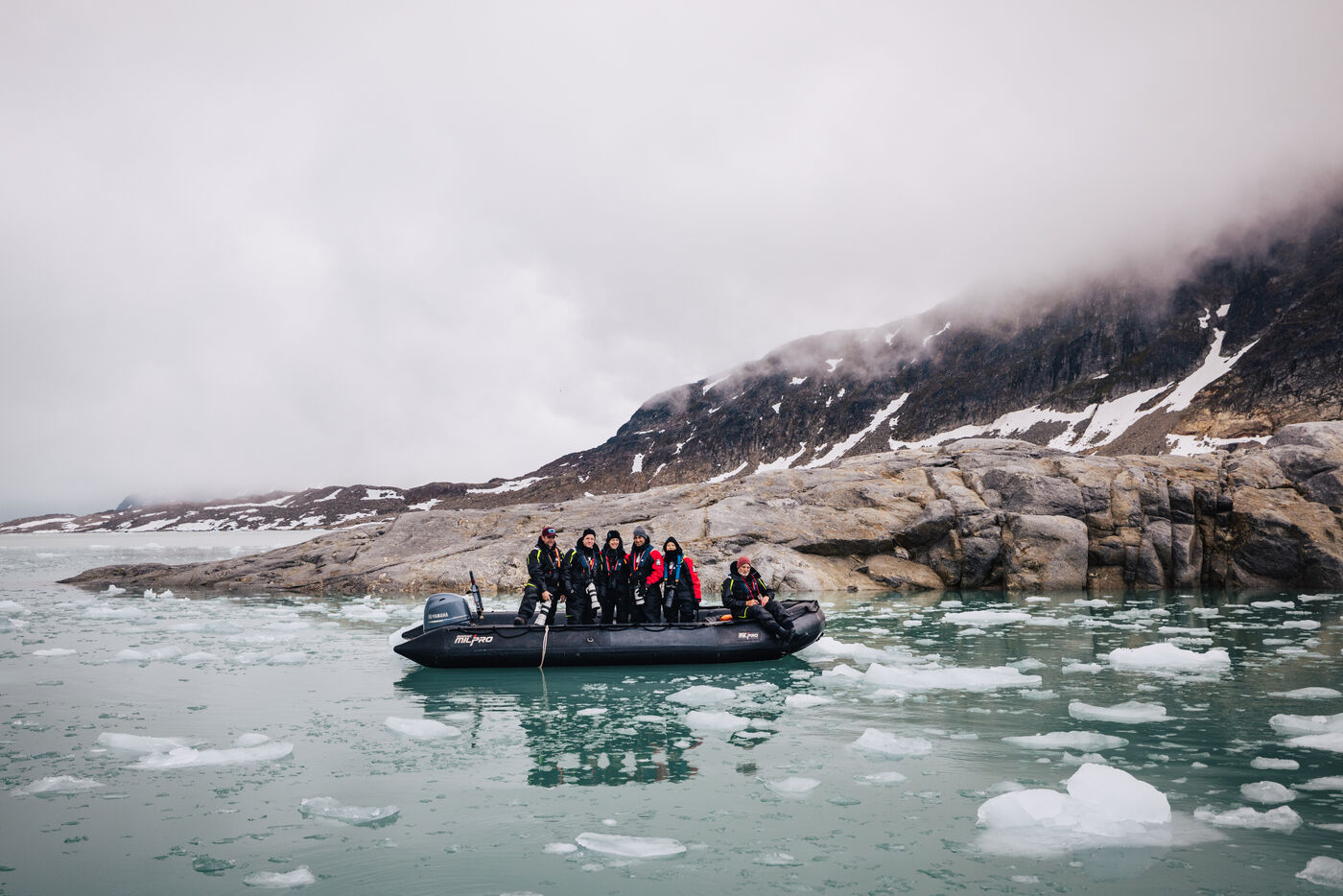Zodiac full of passengers among small ice floes beneath a rocky shore