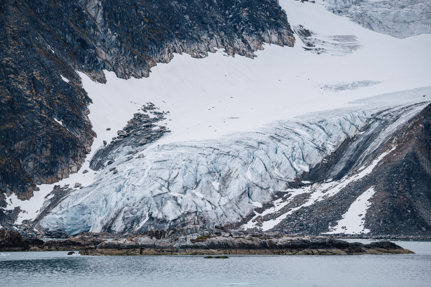 Glacier tongue flowing down between dark rock walls to the shore