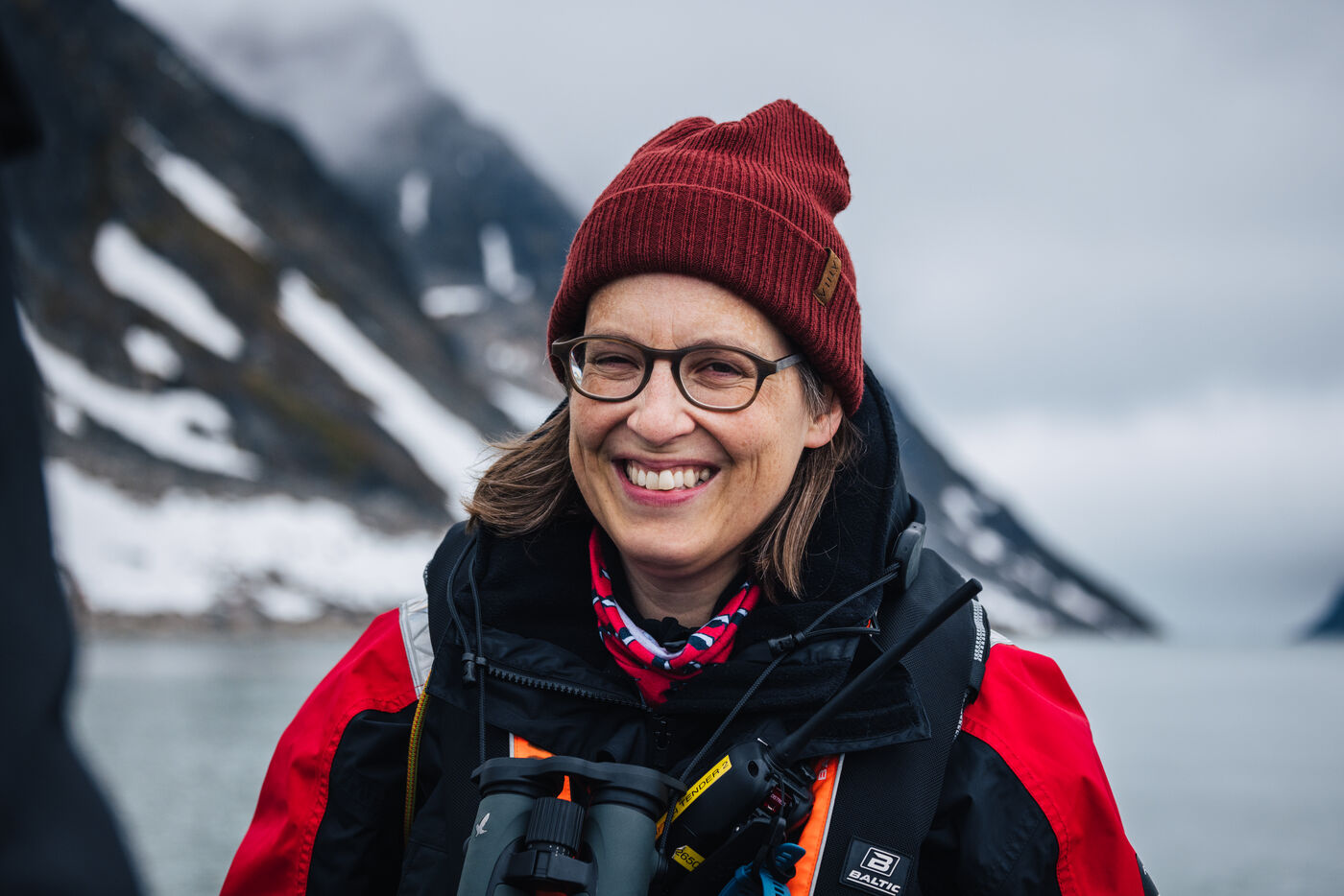 Smiling woman in a red beanie and glasses with binoculars around her neck