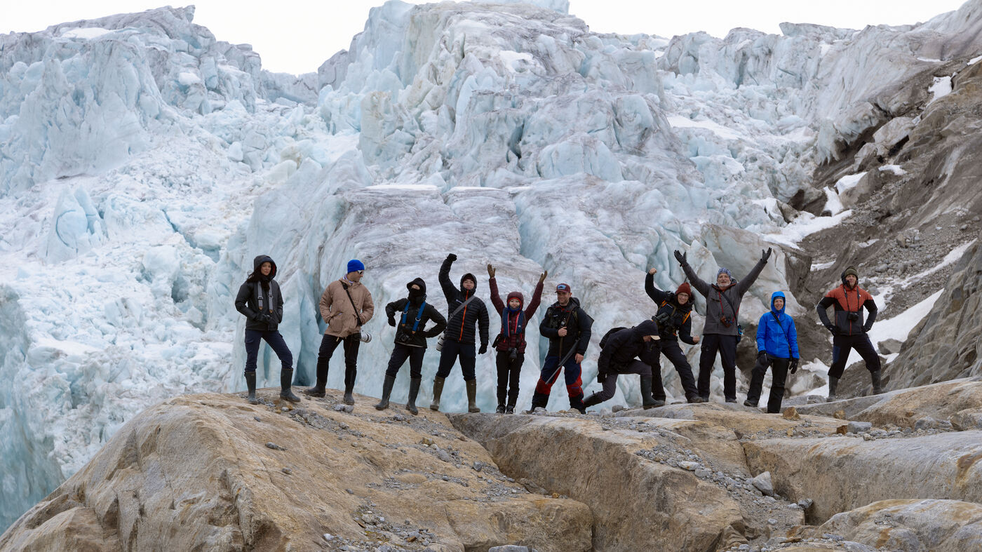 Group of explorers celebrating at the base of a massive glacier
