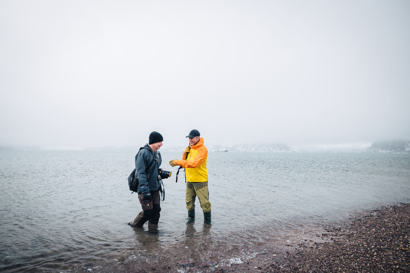 Two people wading in shallow water with misty mountains behind