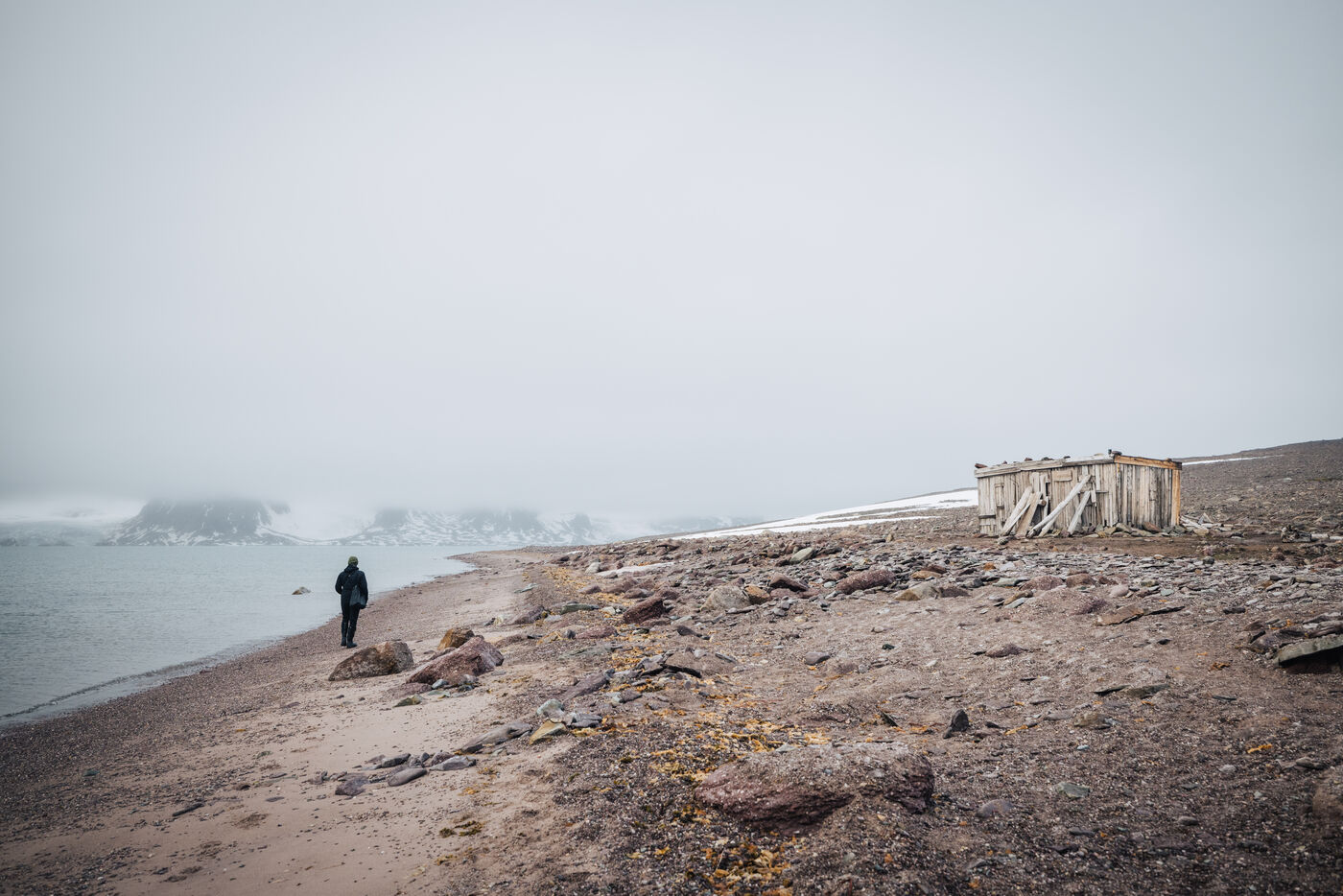Solitary figure on rocky beach with abandoned wooden structure