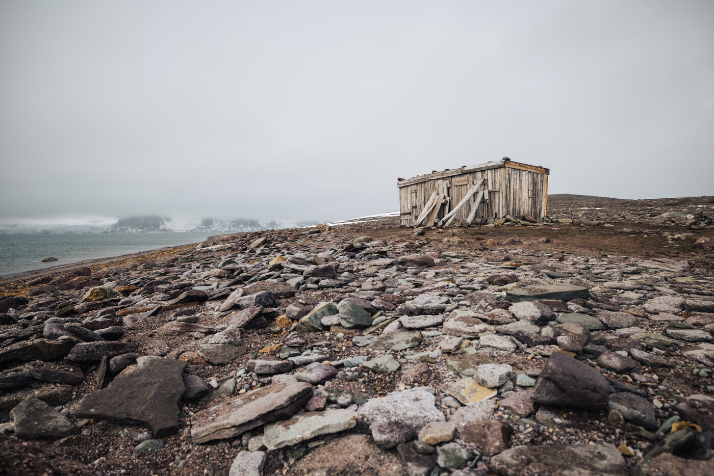 Weathered wooden building frame on barren landscape with distant glaciers