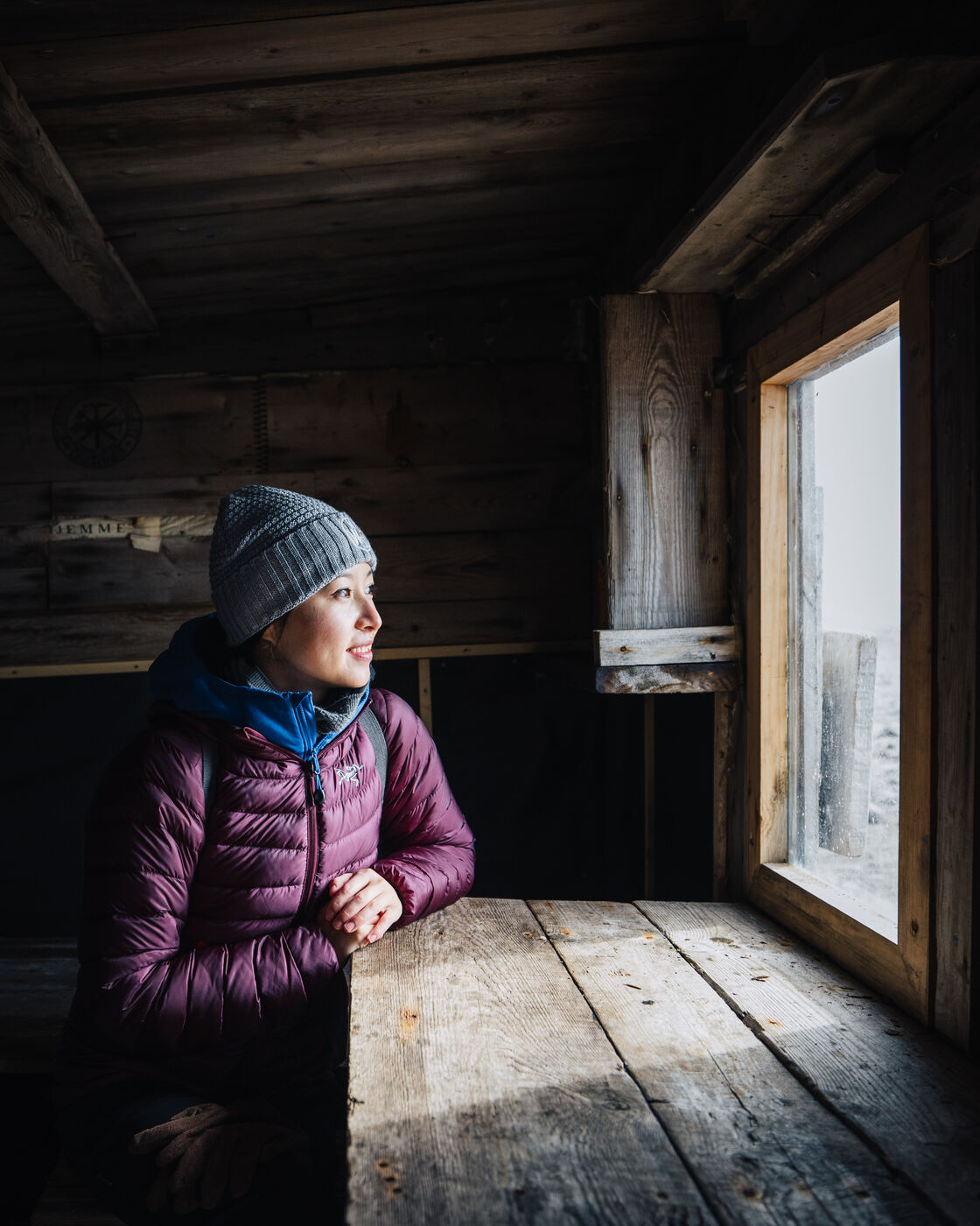 Woman gazing out a window inside a dark wooden cabin