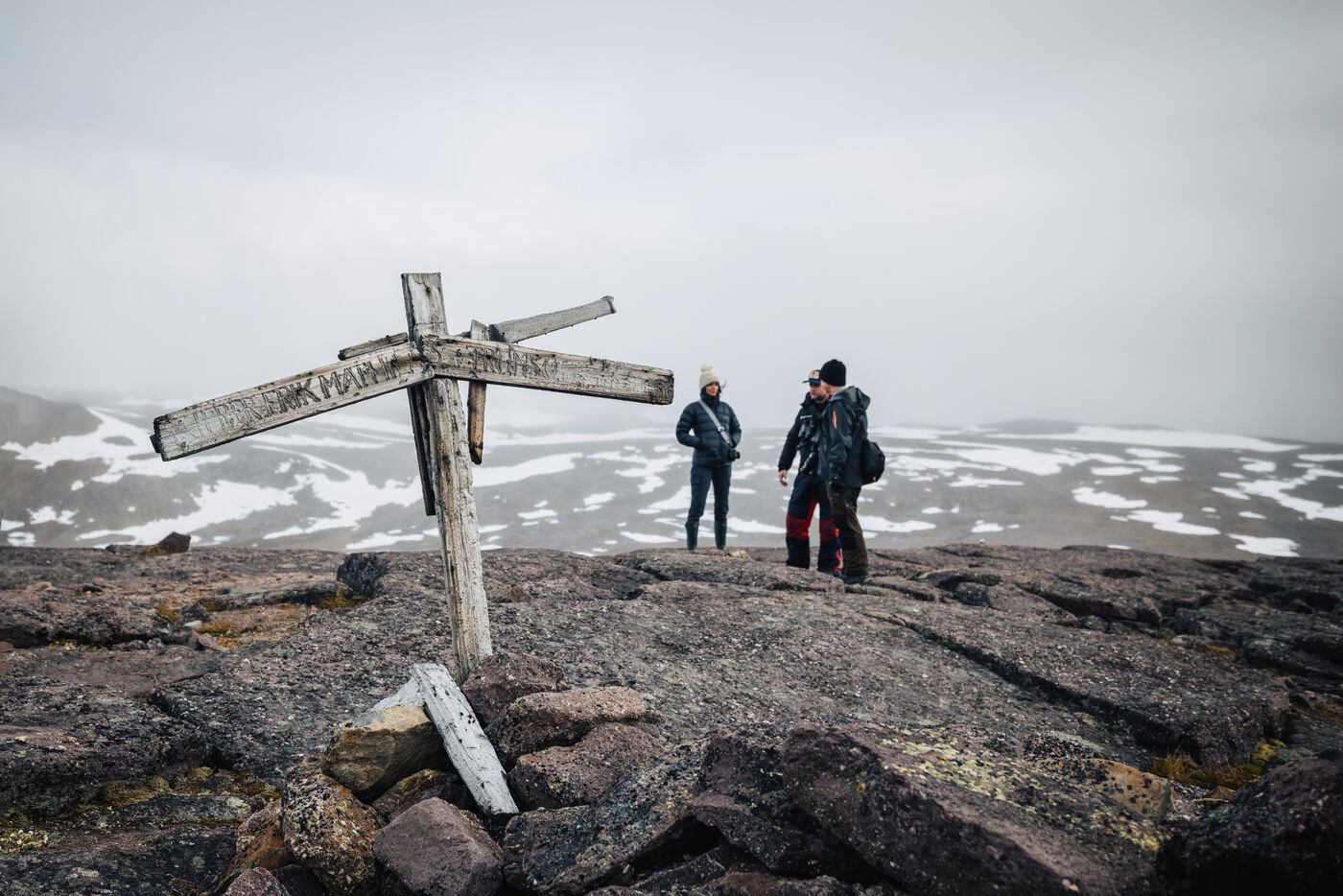 Two hikers near a weathered wooden cross on a barren ridge