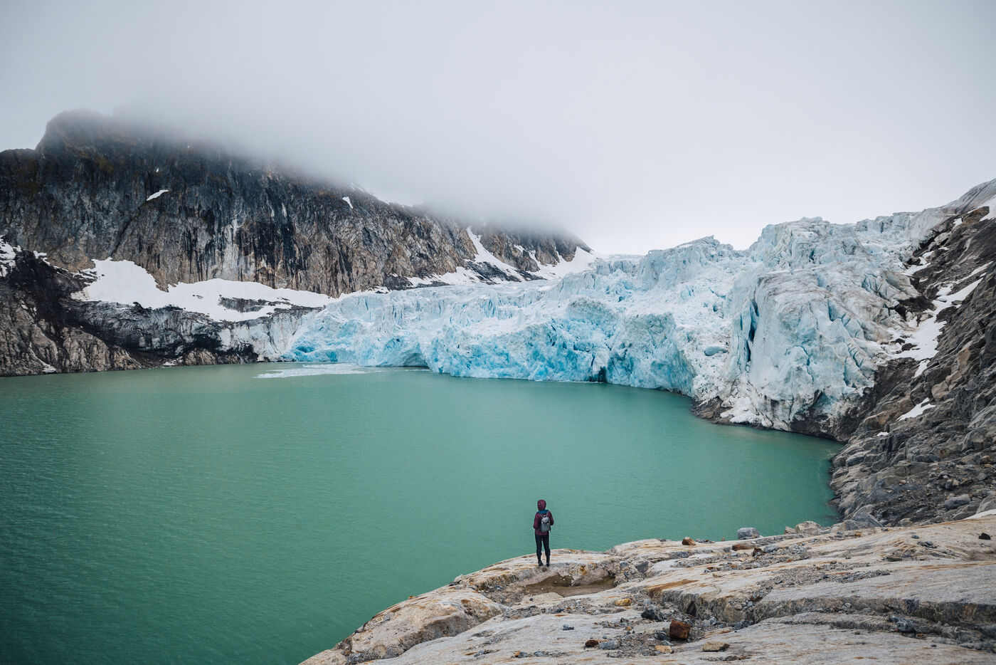 Person standing on rock above a turquoise glacial lake beneath the glacier front
