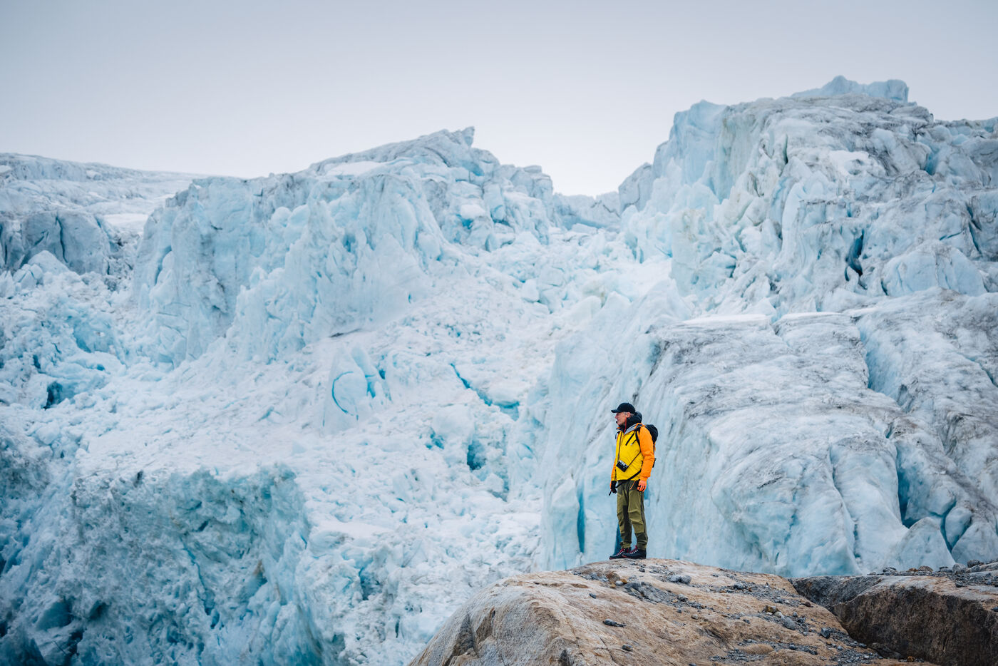 Person standing on rocky ground with massive turquoise glacier face behind