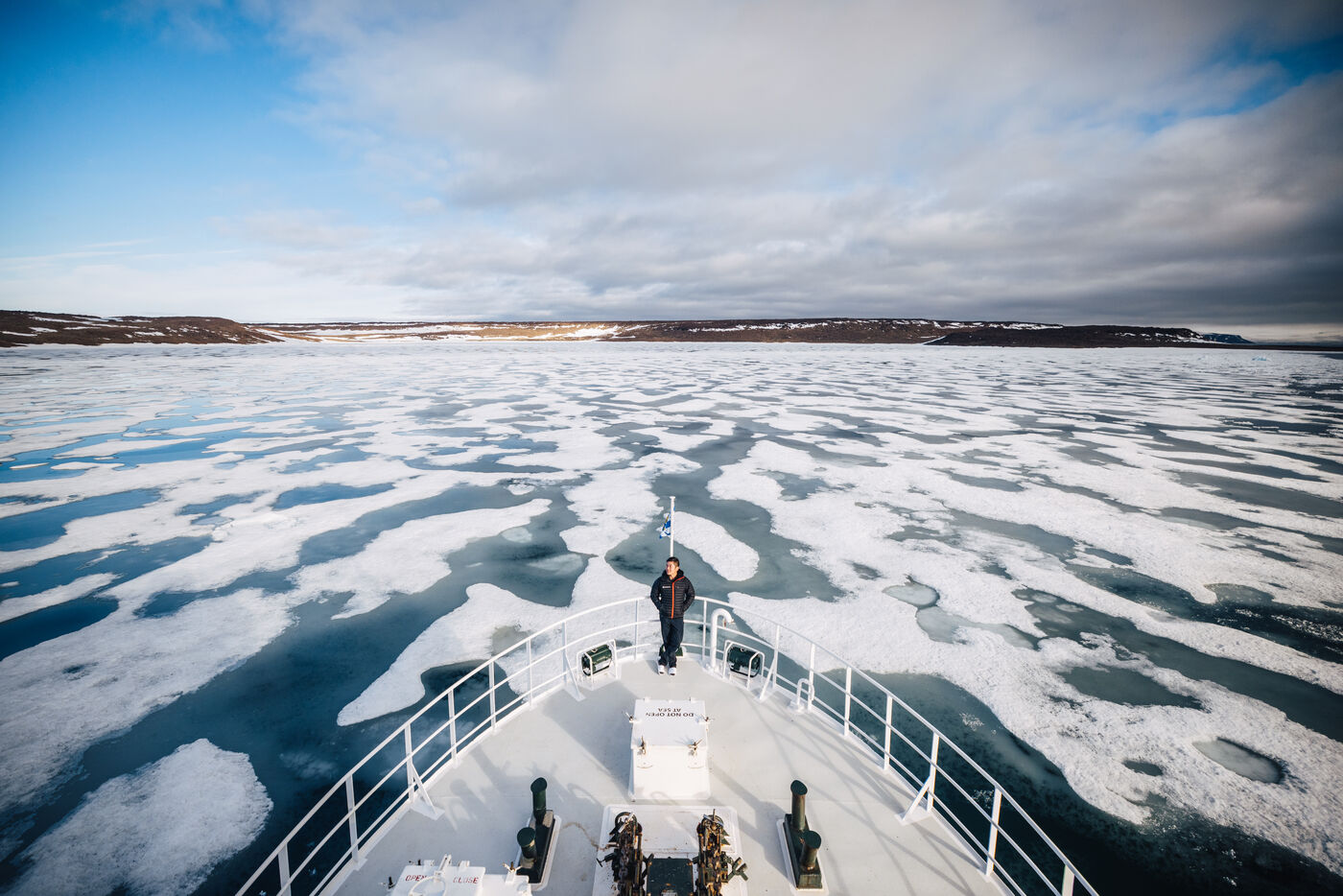 Passenger standing at the bow of the Kinfish as it pushes through broken sea ice