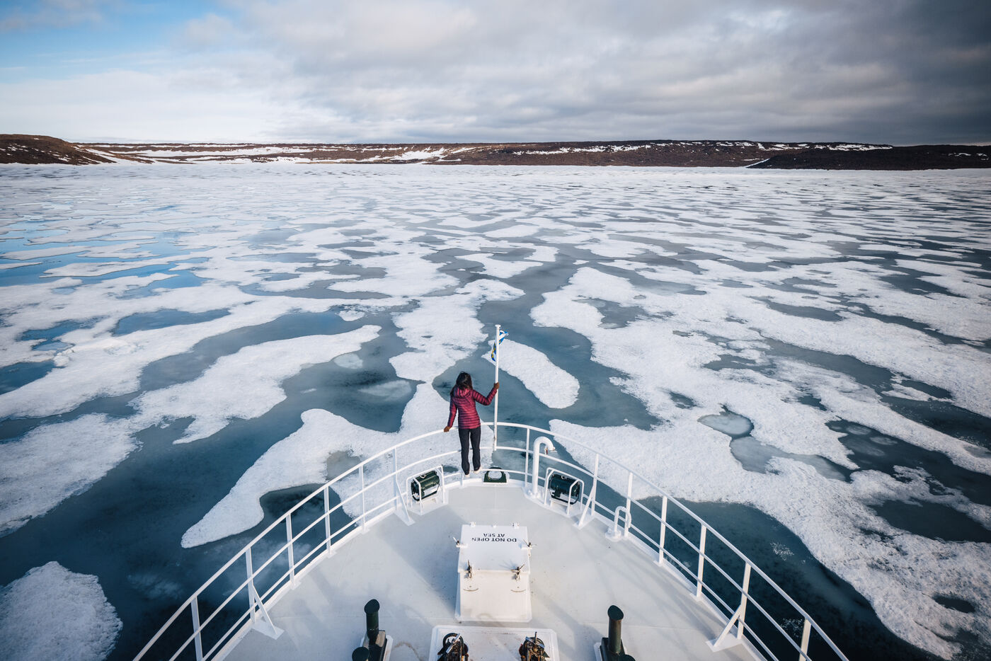 Person in a red jacket at the bow of the Kinfish as it pushes through pack ice